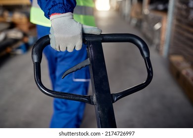 Close up of warehouse worker using pallet jack while working at storage compartment. 