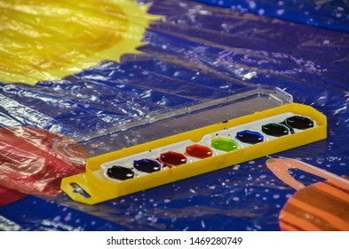 Close Up Of Water Color Paints Set Yellow And White Tray Rainbow Of Oval Paints On Space Themed Plastic Table Cloth