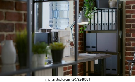 Close Up Of Water Cooler And Coffee Machine On Table Used By People For Refreshment On Break. Modern Equipment And Accessories For Fresh Beverage On Desk In Brick Wall Office.