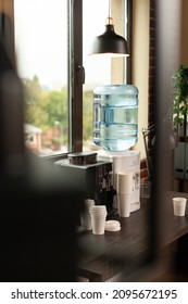 Close Up Of Water Dispenser On Table In Workplace At Office. Water Cooler And Coffee Machine Prepared For People Using Modern Space With Decorations. Beverage And Refreshment In Brick Wall Room.