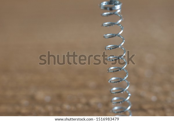 Close up water drop on metal\
spring isolated on wooden background,Sensitive\
focus