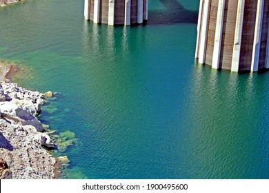 Close Up Of Water And Intake Towers At Hoover Dam. Green And Turquoise Water With Some Rocks And Stones.