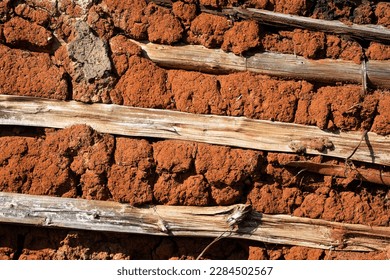 Close up of a wattle and daub wall of a rural hut made of red clay and wood. 