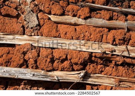 Close up of a wattle and daub wall of a rural hut made of red clay and wood. 