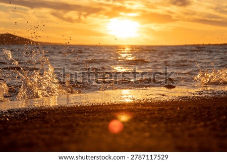 Close up of wave splashing the beach and creating natural water sculptures,  at the end of a summer day during the golden hour as the sun shines on the yellow cloudy sky upon the shuffled sea, the shore and waves