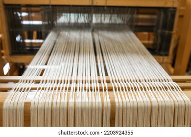 Close Up Of Weaving Machine. A Loom Machine For Clothing Or Woven Label. Weaving Machine For Garment Industry. Yarn Thread Lines On The Weaving Loom Machine For Clothing In Textile Factory.