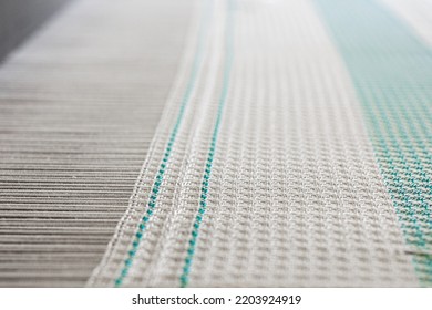 Close Up Of Weaving Machine. A Loom Machine For Clothing Or Woven Label. Weaving Machine For Garment Industry. Yarn Thread Lines On The Weaving Loom Machine For Clothing In Textile Factory.