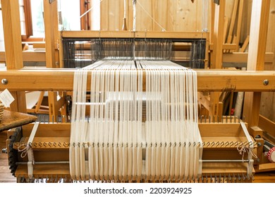 Close Up Of Weaving Machine. A Loom Machine For Clothing Or Woven Label. Weaving Machine For Garment Industry. Yarn Thread Lines On The Weaving Loom Machine For Clothing In Textile Factory.