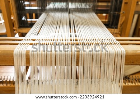 close up of weaving machine. A loom machine for clothing or woven label. Weaving machine for garment industry. Yarn thread lines on the weaving loom machine for clothing in textile factory.