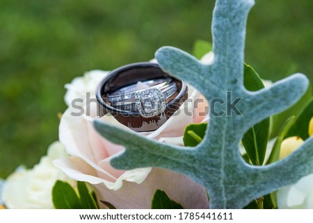 Close up of wedding rings resting on bridal bouquet view through greenery bokeh effect Background outdoors grass