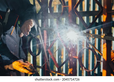 Close Up Of A Welder Hands Welding Steel Structure Metal Part In Home Backyard. Craft Man Use Electric Arc Argon Wear Work Uniform,protective Helmet On Head Without Gloves While Sparks Fly At Factory.