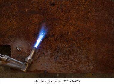 Close up welder torch hose with fire on rusty steel sheet
