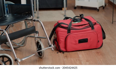 Close Up Of Wheelchair And Nursing Bag On Floor Of Nursing Home. Carrier With Medical Equipment And Devices For Healthcare Treatment And Assistance. Objects For Rehabilitation Service