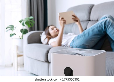 Close up of white air purifier on the floor in living room the background of young Asian woman lie down. Concept of caring for fresh air at home. Caring for well-being and health. Air filter.