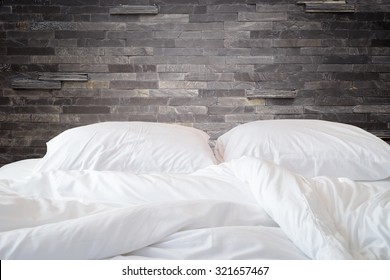 Close Up White Bedding Sheets And Pillow On Natural Stone Wall Room Background, Messy Bed Concept