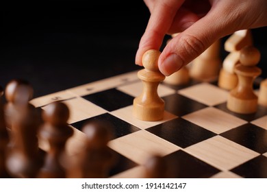 Close Up Of White And Black Wooden Chess Pieces On Board. Woman's Hand Makes First Move Of White Pawn On Chessboard. Concept Of Intelligent, Logical And Strategic Game