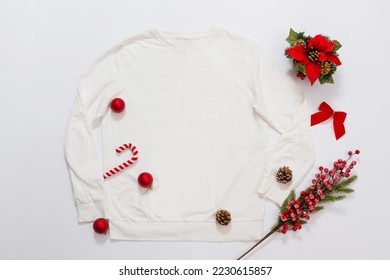 Close up white blank template sweatshirt copy space. Christmas Holiday concept. Top view mockup sweatshirt. Red holidays decorations on white background. Happy New Year accessories. Xmas outfit