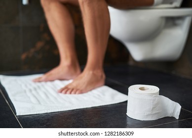 Close Up Of White Bog Roll On The Floor Of Lavatory. Gentleman Locating Bare Legs On Carpet