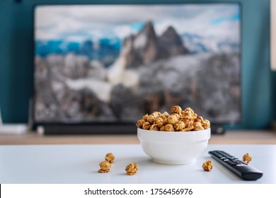 Close Up Of A White Ceramic Bowl Of Caramel Popcorn And Remote Control For Smart TV. Home Cinema And Watch Ing A Movie Or Series At Home Concept.