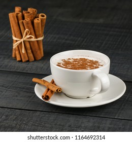 Close up white cup of salep milky hot drink of Turkey with cinnamon powder healthy spice on black wooden background