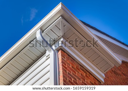 Close up of white frame gutter guard system, eaves through, fascia, drip edge, colonial white soffit with ventilation, brick facade siding on a luxury American single family home neighborhood USA