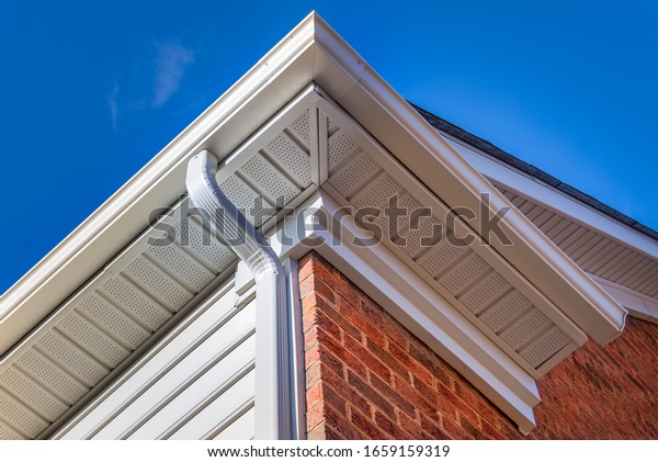 Close up of white frame gutter guard system, eaves\
through, fascia, drip edge, colonial white soffit with ventilation,\
brick facade siding on a luxury American single family home\
neighborhood USA
