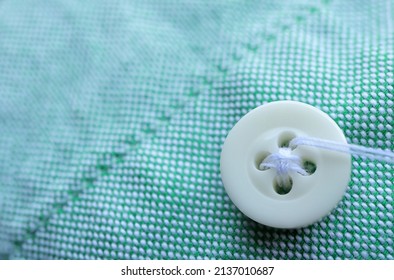 Close Up Of White  Sewing Button On A Green Shirt. Empty Space For Text. Craft, Needlework Concept.