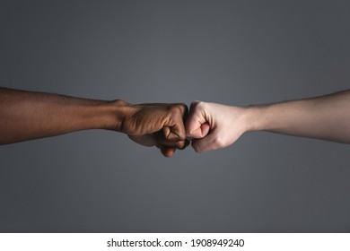 Close up of white skinned man and dark skinned man doing a fist bump isolated on gray background with copy space. - Shutterstock ID 1908949240