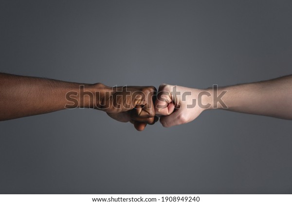 Close up of\
white skinned man and dark skinned man doing a fist bump isolated\
on gray background with copy\
space.