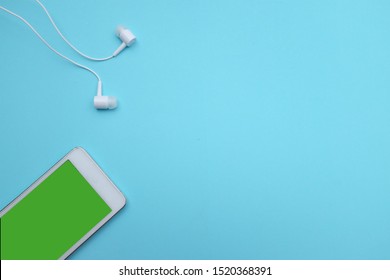 close up white smartphone Green screen on the blue background with headphones.