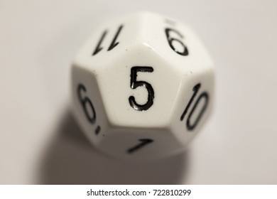 Close up of a white twelve-sided dice, top-down view, with the number one showing.
