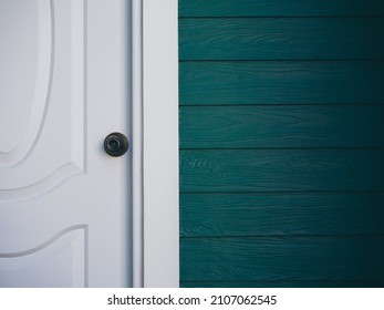 Close up the white vintage clean front door with iron knob near wood plank wall, dark green color with copy space.