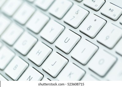Close up of white wireless aluminum keyboard photographed with shallow depth of field.
