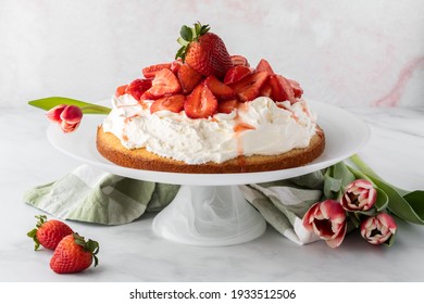 Close up of a whole strawberry shortcake on a cake stand with tulips to the side. A spring food concept.