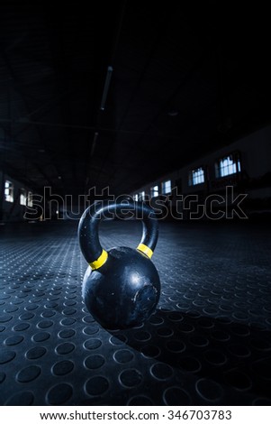 Close up wide angle view of a kettle bell weight on the floor of a gym with moody light.