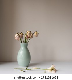 Close up of wilted pink roses in green vase on table against wall (selective focus)