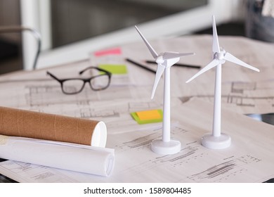 Close up of wind turbines on a table with architectural plan blueprints. Two models of wind turbines on desk with architecture layout and paper. Green and eco sustainable architecture.