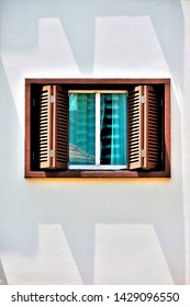 Close Up Of Window With Brown Teak Bi Fold Wooden Shutters With Blue Glass On A White Wall Of House In Singapore With Space For Copy