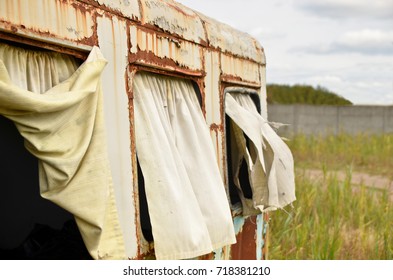 Close up of windows of an old abandoned rusty trailer covered with weathered curtains. 