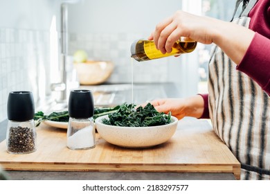 Close up woman adding olive oil while cooking kale chips or healthy salad for dinner on the kitchen table. Healthy eating, dieting lifestyle. Selective focus, copy space. - Powered by Shutterstock