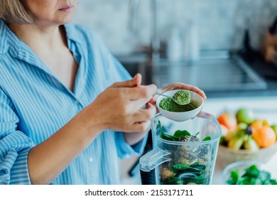 Close up woman adding wheat grass green powder during making smoothie on the kitchen. Superfood supplement. Healthy detox vegan diet. Healthy dieting eating, weight loss program. Selective focus