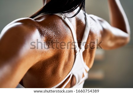 Close up of woman back with flexing her muscles in sweat on skin after workout. Female bodybuilder with perfect biceps                          