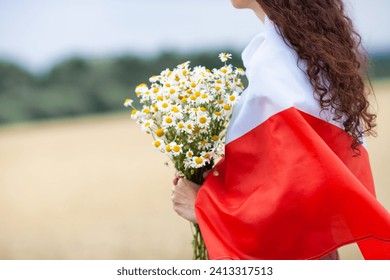 Close up of woman with bouquet of daisies covered with flag of Poland in wheat field. Polish Flag Day. Independence Day. Travel and learn polish language concept.