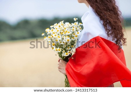 Close up of woman with bouquet of daisies covered with flag of Poland in wheat field. Polish Flag Day. Independence Day. Travel and learn polish language concept.