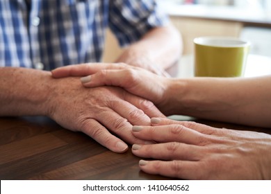 Close Up Of Woman Comforting Unhappy Senior Man Sitting In Kitchen At Home                          