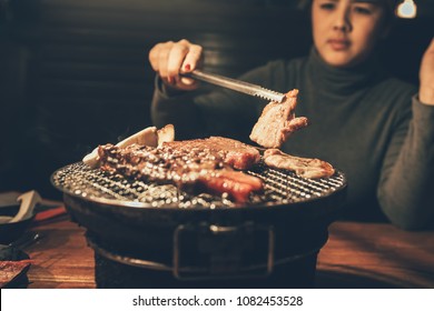 Close up woman cooking pork meat on a charcoal grill in restaurant.