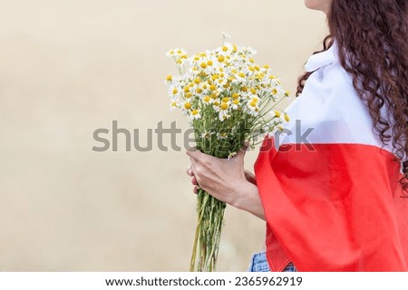 Close up of woman covered with  flag of Poland holding bouquet of daisies in wheat field. Side view. Polish Flag Day. Independence Day. Travel and learn polish language concept.