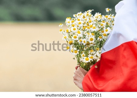 Close up of woman covered with  flag of Poland holding bouquet of daisies. Side view, nature background. Polish Flag Day. Independence Day. Travel and learn polish language concept.