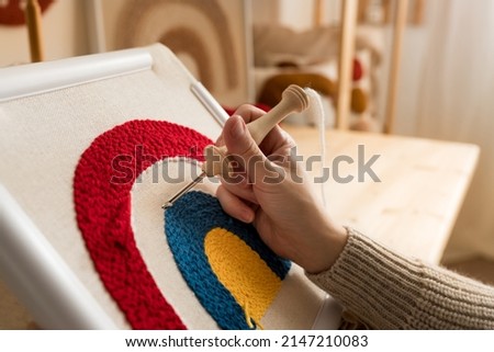 Close up of woman creating a handmade decoration for home. Female pushing the punchneedle straight down into the fabric. Hobby, DIY, handycraft concept. New trend in embroidery Punch needle.