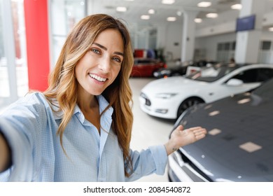 Close Up Woman Customer Buyer Client In Shirt Do Selfie Shot Pov On Mobile Phone Point Hands On Car Choose Auto Want Buy New Automobile In Showroom Vehicle Salon Dealership Store Motor Show Indoor.